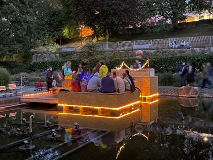 beleuchtetes Holz-Podest, auf dem Menschen sitzen, auf dem Brunnen im Kurpark