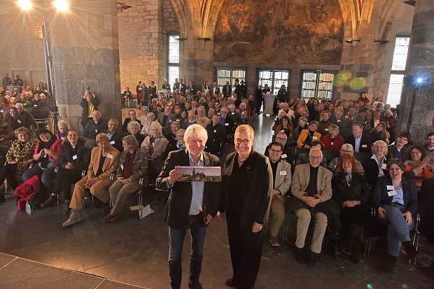 Oberbürgermeisterin Sibylle Keupen bedankt sich bei Jürgen Becker. Im Hintergrund sitzen die Gäste.