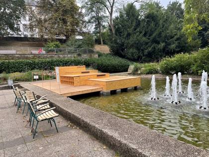 aufgebautes Holz-Podest auf Brunnen im Kurpark, daneben eine Stuhlreihe